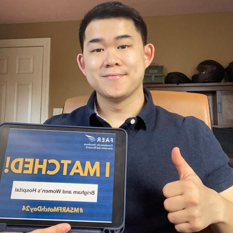 A man poses for a selfie holding a tablet displaying the words "I Matched!一边竖起大拇指